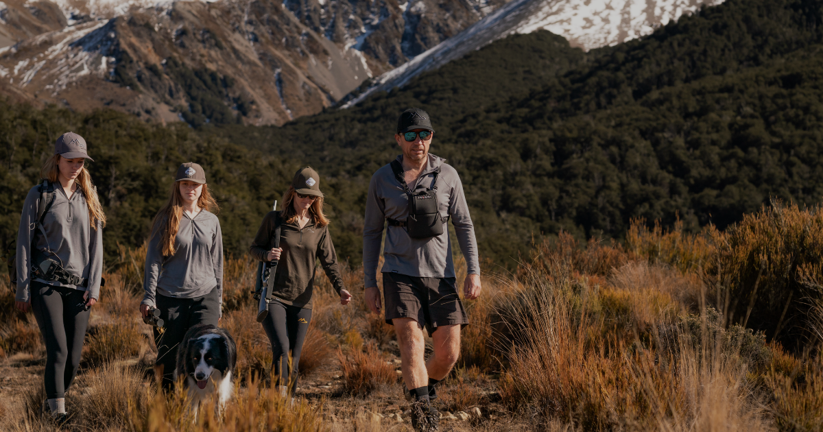 Family hiking in Main Divide merino apparel through tussock terrain with snow-capped New Zealand mountains in the background