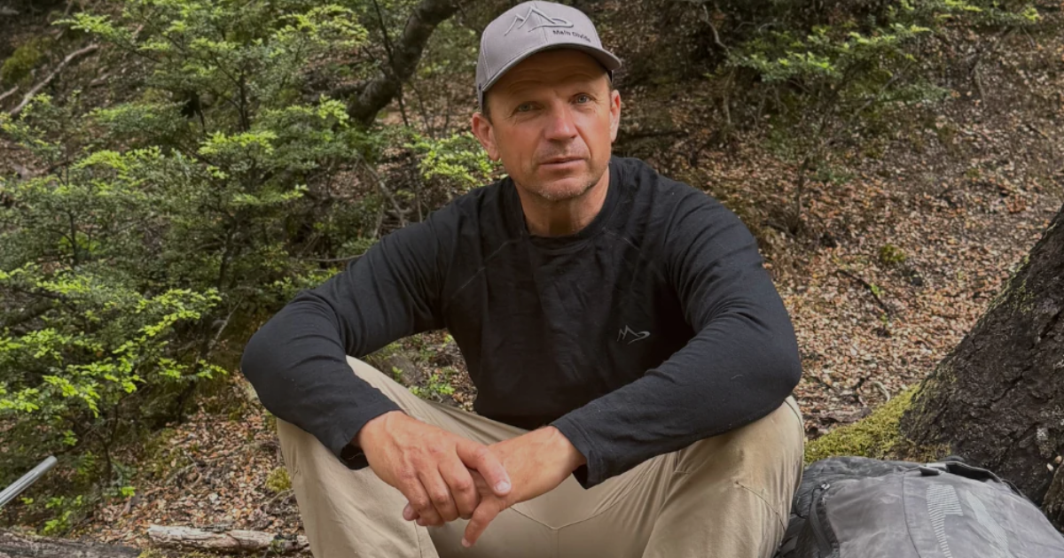Man wearing Main Divide merino long-sleeve top and cap resting against a tree in New Zealand bush