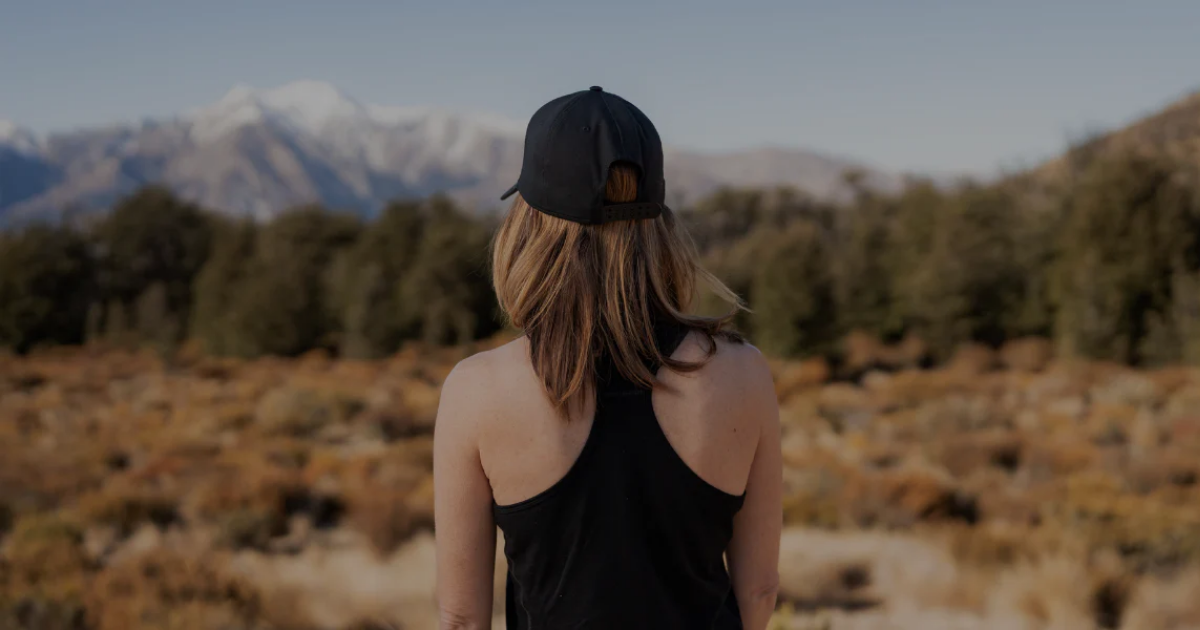 Woman wearing a Main Divide merino singlet and cap looking out over tussock flats towards snow-capped New Zealand mountains