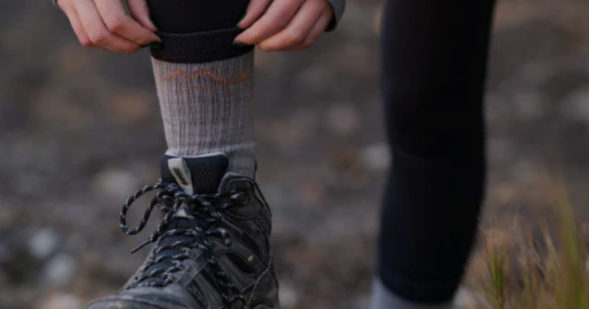 Close-up of Main Divide merino hiking socks being pulled up over a hiking boot on rocky terrain