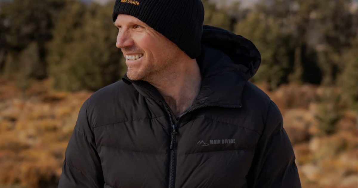 Man wearing the Main Divide Ranger Down Puffer Jacket in black, smiling in New Zealand backcountry terrain